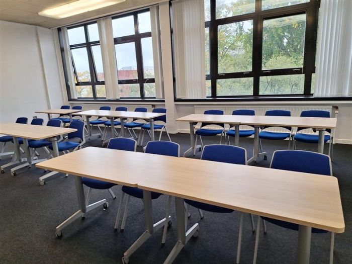 Flat floored teaching room with rows of tables and chairs, and whiteboard.
