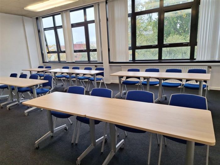 Flat floored teaching room with rows of tables and chairs.