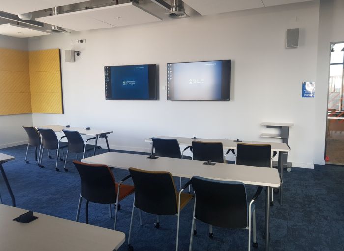 Flat floored teaching room with rows of tables and chairs, and two large screens.