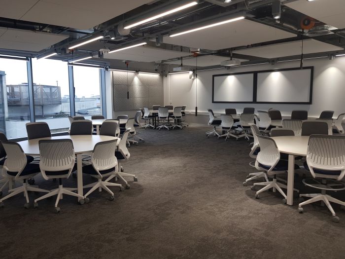 Flat floored teaching room with tables and chairs, and two large screens.