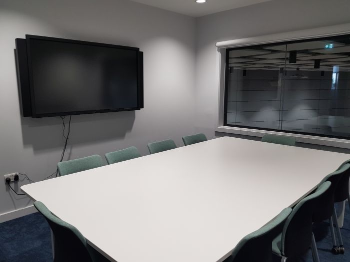 Flat floored teaching room with table and chairs, and large screen.