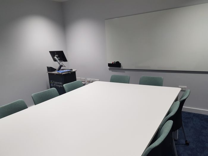 Flat floored teaching room with table and chairs, PC, lectern, and whiteboard.