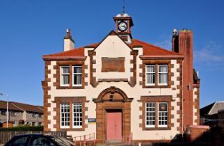 A old building with red sandstone, white harling (pebble dash) with a red front door, four lage windows and a small clock tower on top. Image source: James Galt published on Flickr (CC BY-ND 2.0) https://www.flickr.com/photos/32051939@N00/3144655107 