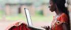 A black African woman in a red and yellow dress sitting with her back against a tree and looking at a laptop resting on her knees. Source: iStockPhoto https://www.istockphoto.com/photo/technology-symbol-african-woman-studying-learning-lesson-gm529835071-54284780