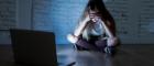  A young girl sitting crosslegged on the floor with her head in her hands, lit by the glow from the open laptop on the the floor beside her. Source: SB Arts Media | iStockphoto https://www.istockphoto.com/photo/scared-sad-girl-bullied-on-line-with-laptop-suffering-cyberbullying-and-harassment-gm964741476-263339312 