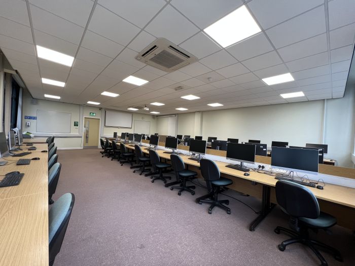 Flat floored teaching room with rows of PCs and monitors, whiteboards and large screen.