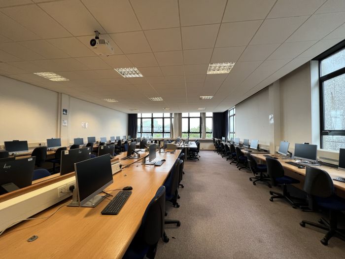 Flat floored teaching room with rows of PCs and monitors, and projector..