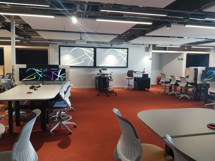 Flat floored Teach Enabled Active Learning (TEAL) room with tables and chairs in groups, each with accompanying monitors, PC, lectern, lecturer's chair, and two large screens.