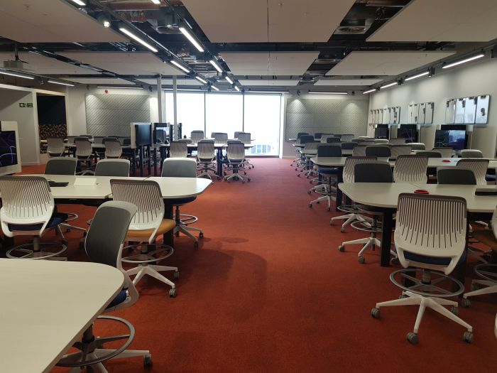 Flat floored Teach Enabled Active Learning (TEAL) room with tables and chairs in groups, each with accompanying monitors, and handheld whiteboards.