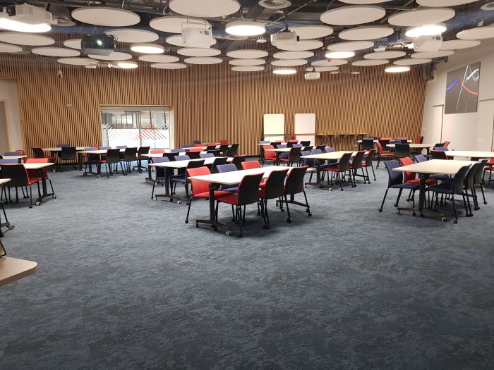 Flat floored teaching room with tables and chairs in groups, large screen, and whiteboards.