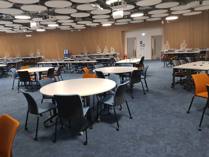 Flat floored teaching room with tables and chairs in groups.