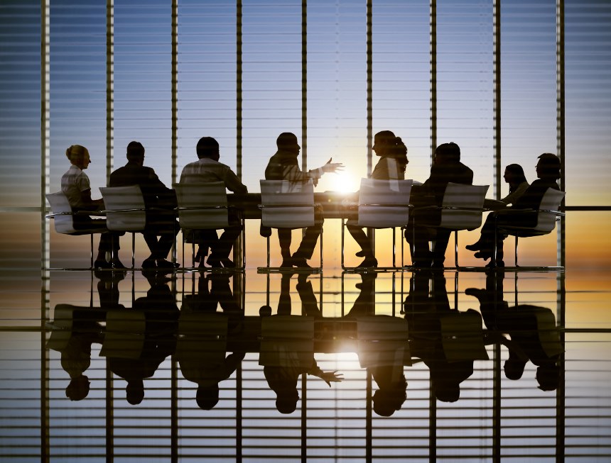 An image showing a silhouette of a group sat at a table in an office with a glass window