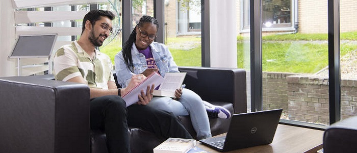 Two students collaborating in the library cafe by making notes from books and a laptop. Source: GU Image Library