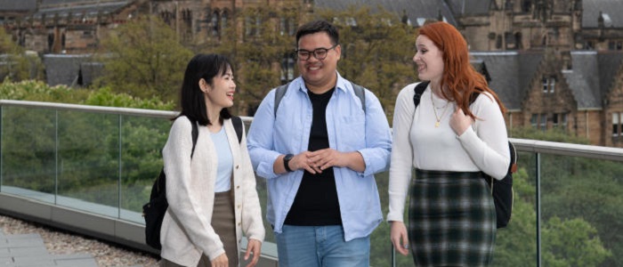 Three students chatting on the viewing deck of the James McClune Smith Building with old university buildings behind them. Source: GU Image Library