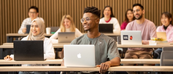 Smiling students with laptops in rows in a lecture hall. Source: GU Image Library