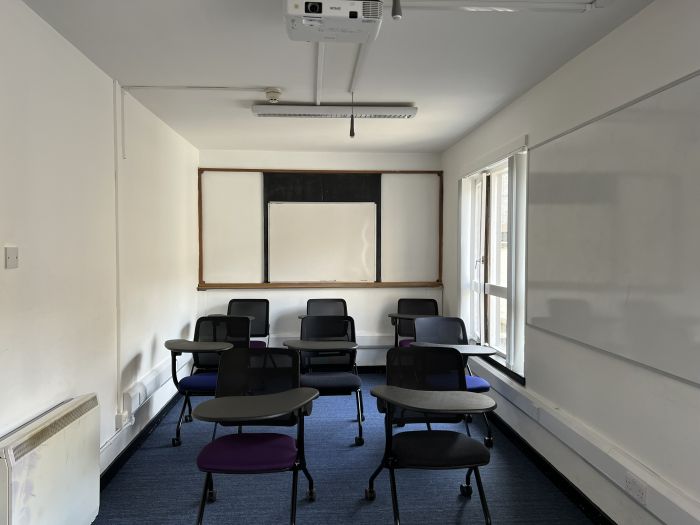 Flat floored teaching room with tablet chairs, whiteboards and projector.