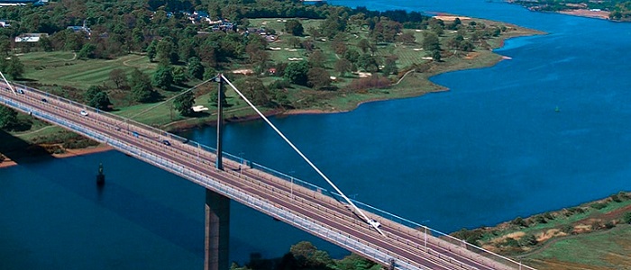 A road bridge over a river that flows into a wider, winding estuary in the distance