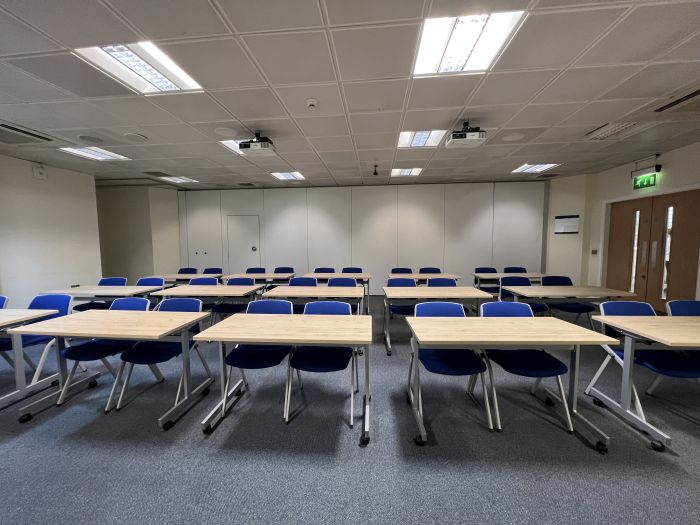 Flat floored teaching room with rows of tables and chairs, and projectors.