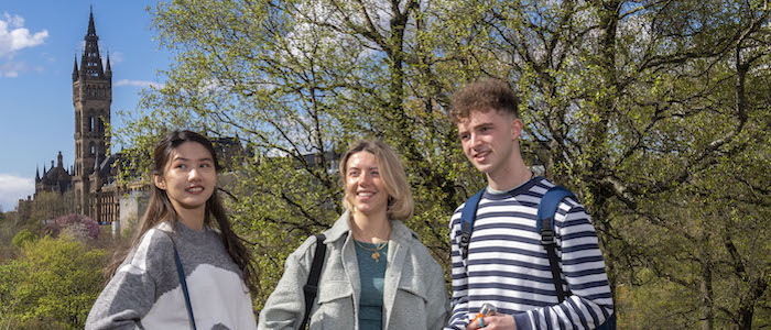 Three students in a Kelvingrove Park with trees and the Glasgow University tower in the background. Source: GU Image Library