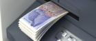 Lots of twenty pound notes coming out of a cash machine slot, showing an illustration of economist Adam Smith