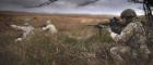 Soldier crouching on a grassy moor and aiming a gun, with two other soldiers in the background doing the same. Image credit: Photographer: Corporal Tom Evans (RLC) | UK MOD © Crown copyright 2019 | Open Government License  https://www.flickr.com/photos/defenceimages/32776552298 www.nationalarchives.gov.uk/doc/open-government-licence/version/3/