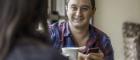 A man smiling as he enjoys a conversation and coffee with another person. Image credit: JasonDoiy | iStockphoto https://www.istockphoto.com/photo/good-friends-and-good-coffee-gm529080351-54274924
