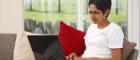 A woman reclined on a sofa using a laptop