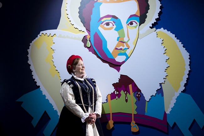 An image of an actor dressed as Mary Queen of Scots in front of The Afterlife of Mary Queen of Scots exhibition