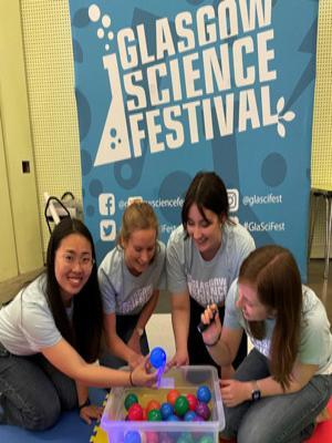 Photograph of four GSF in action students with a colourful mat, bouncy balls and a UV light ready to start the activity.