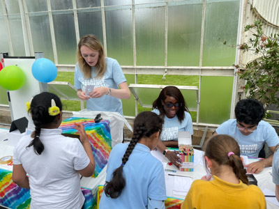 Photograph showing 2 GSF in Action students assisting school children with making paper glasses, whilst another GSF student is in discussion with another school child. 