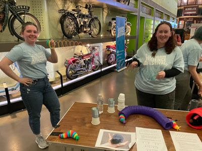 Photograph of two GSF in Action students holding a colourful spring representing sound waves, surrounded by toy worms and tubes to represent underground creatures.. 