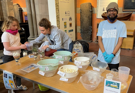 Photograph of two GSF in Action students with a child pouring water into a bottle to learn about water filtration using popcorn and sugar. 