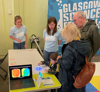 Photograph showing two GSF in Action students with two adults and a child. The child is playing with a UV light. 
