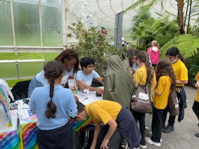 Photograph showing three GSF in Action students assisting several schoolchildren with creating rainbow glasses. 