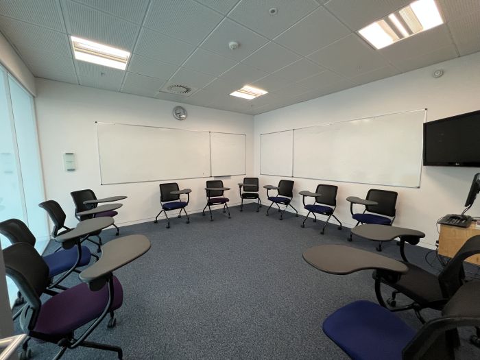 Flat floored teaching room with tablet chairs, whiteboards, video monitor, and PC.