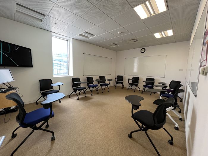 Flat floored teaching room with tablet chairs, whiteboards, video monitor, and PC..