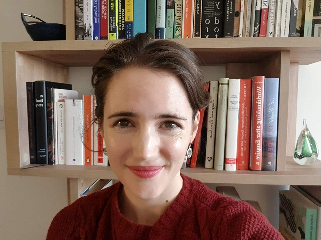 An image of Dr Sarah Dunstan sitting in front of a set of shelves filled with books