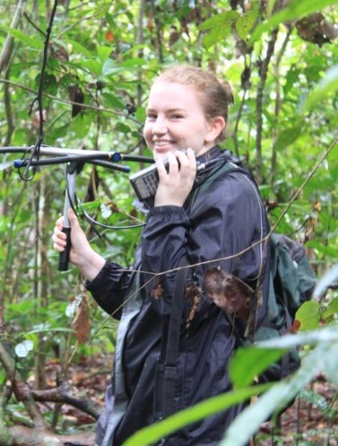 A student smiling into the camera, the background is a jungle.
