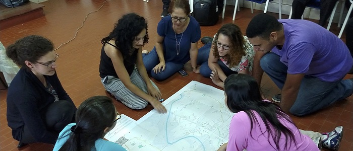 A group of people sitting on the floor examining a map and talking about it