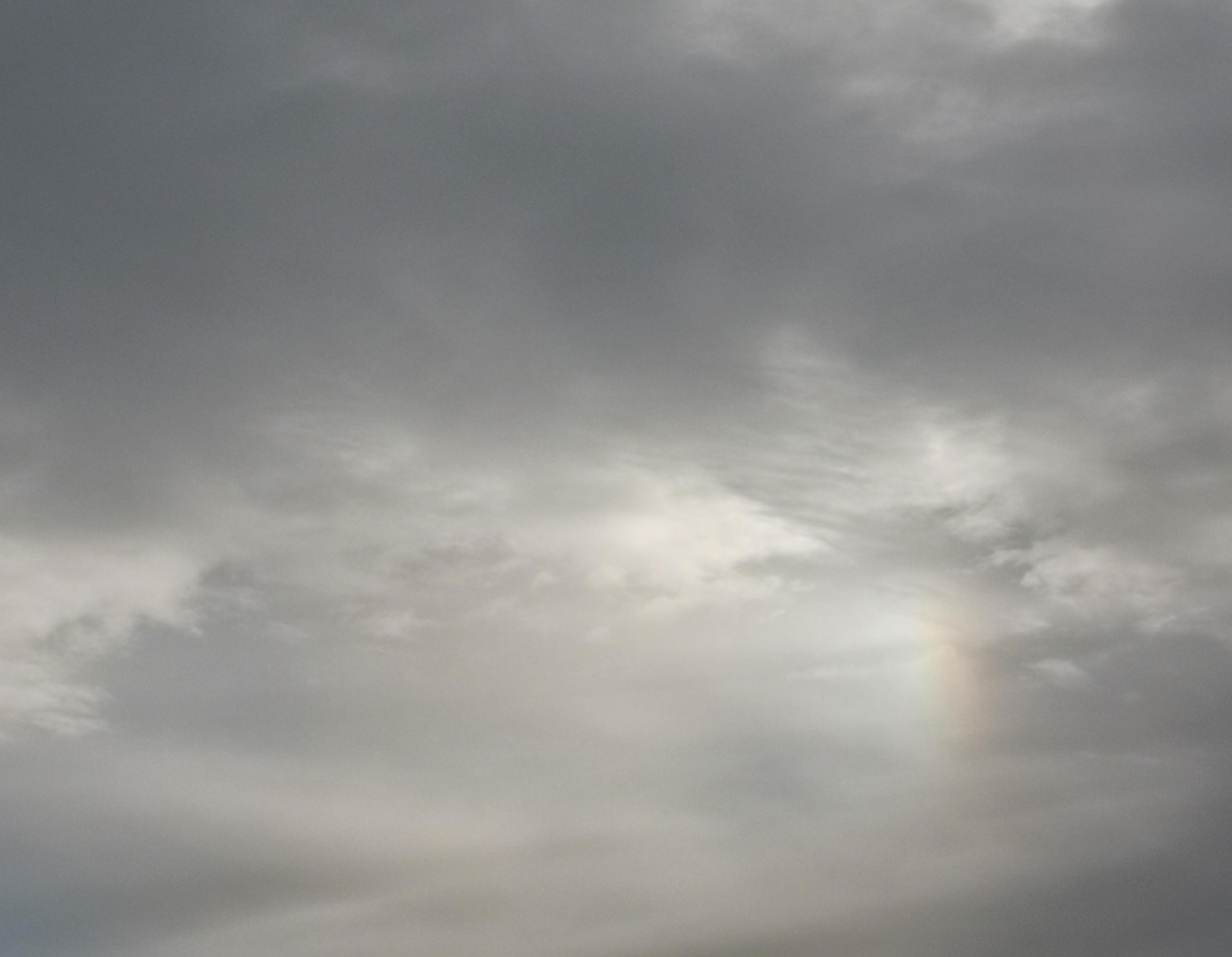a scale of rainbow shows where the sun sits behind a wall of grey clouds in winter