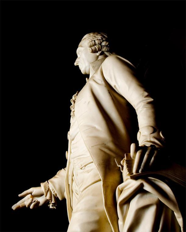 Side view of a white marble statue of Adam Smith against a black background. Source: Glasgow University