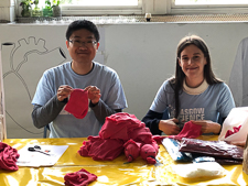 Photograph of two GSF in action students holding materials sat behind a table covered in plush hearts. 