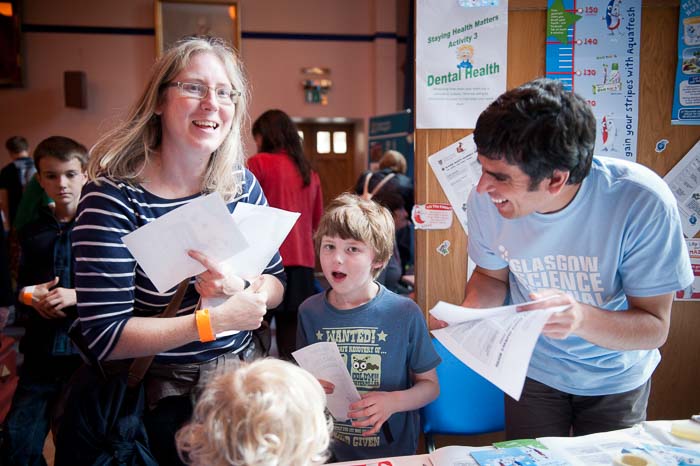 Photograph showing a GSF in Action student with a family. Behind them are posters about dental health. 
