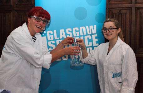 Photograph showing two GSF volunteers in lab coats holding conical flasks.