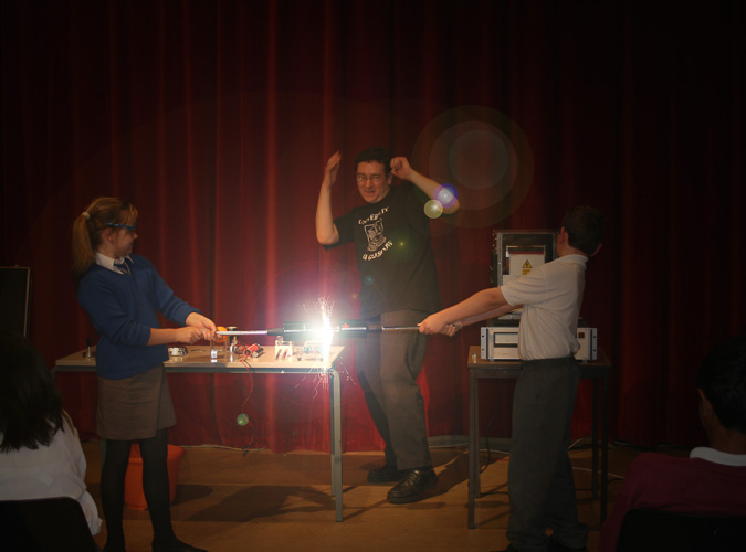 Photograph showing two children holding two electronic rods together to create a bright spark. 