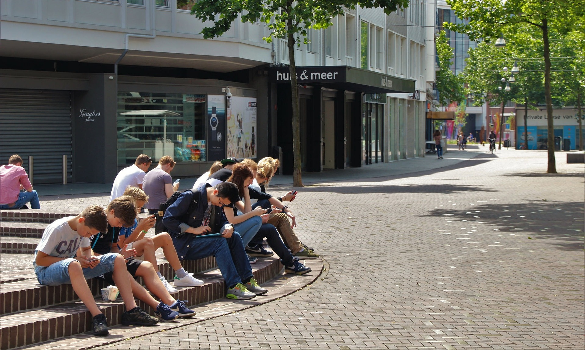 A group of high school students sit outdoors concentrating on their mobile phones