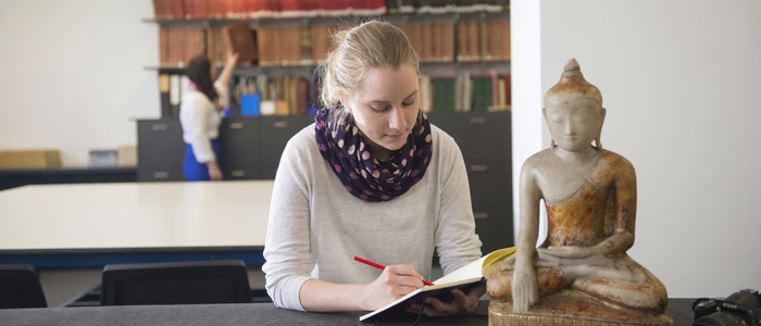 A student writing in a book beside a buddha