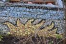 A photo of a mosaic showing a blazing sun against a blue sky in small tiles found in a Glasgow community garden
