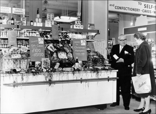Photograph of salesman in the Grocery Department showing a customer a bottle of champagne, c1965.
(GUAS Ref: HF 51/6/1/5/7 photo 2. Copyright reserved.)