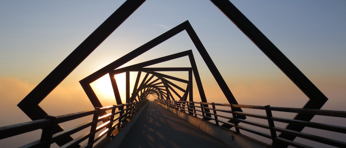 A long pier in the sunset with a square sculpture overhead